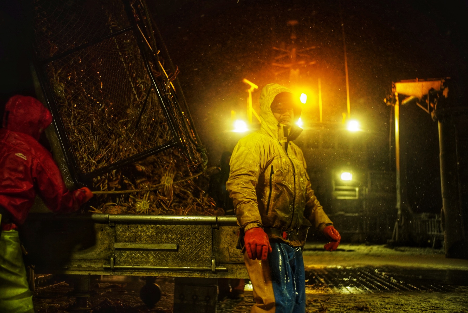 Deck crew hauling a crab pot under amber work lights at night