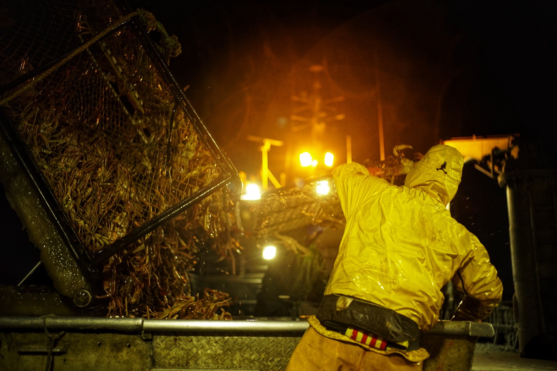 A deckhand guiding a crab pot under night work lights