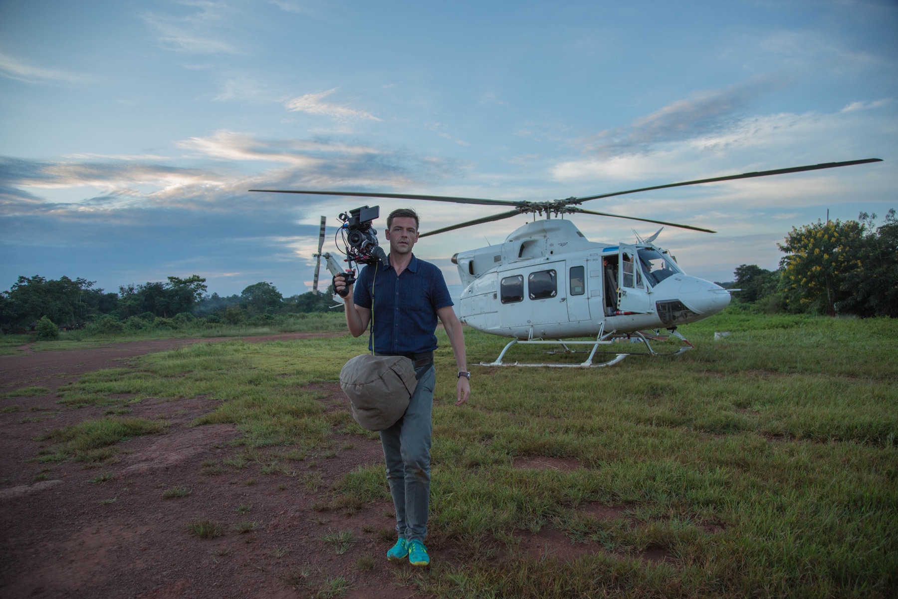 J.J. Kelley carrying a cinema camera in front of a helicopter in Central Africa